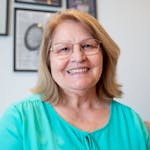 Cheerful senior woman with glasses smiling warmly indoors in Portugal.