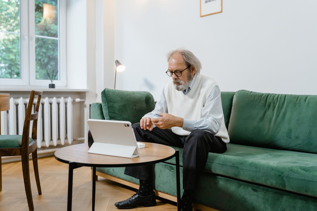 Elderly man engaged in online health consultation using a pulse oximeter and tablet.