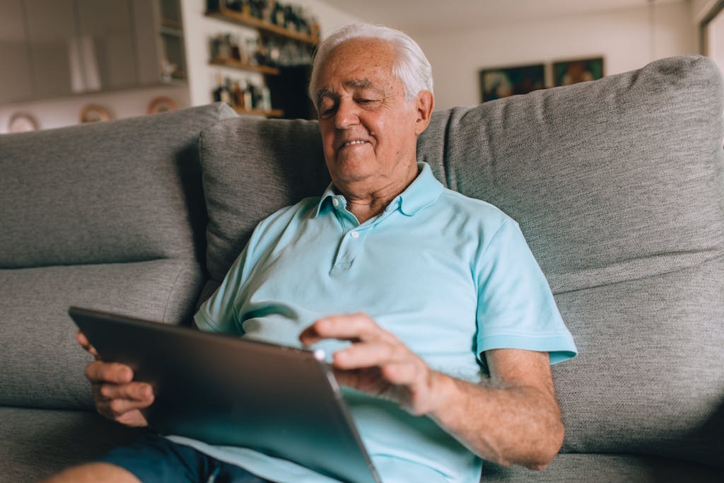 Elderly man enjoying leisure time using a tablet at home.